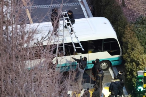 A police officer sets up a ladder to climb over a car wall at the entrance of the presidential residence