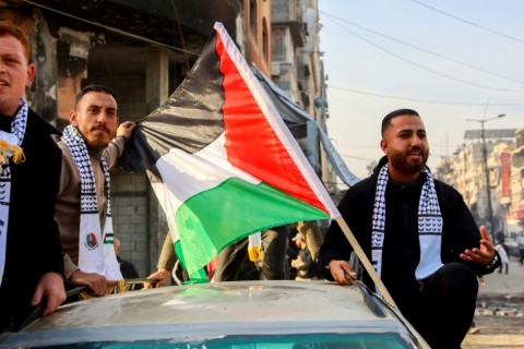 Men ride in a car adorned with a Palestinian flag along a street in Gaza City to celebrate the truce