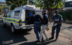 South African Police Service (SAPS) officers leads a man to the back of a police vehicle in Sunnyside, Pretoria.