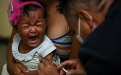 A girl accompanied by her mother receives a dose of measles and rubella vaccine from medical personnel at a community health center in the Lidice neighborhood in Caracas