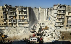 Syrian soldiers look on as rescuers use heavy machinery sift through the rubble of a collapsed building in the northern city of Aleppo