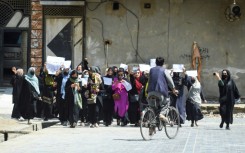 Afghan burqa-clad women walk past a Taliban security personnel along a street in Jalalabad, Afghanistan