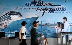 People walk past a billboard at the passenger transportation center of Qingdao Cruise Terminal in Qingdao. Li Ziheng/Xinhua via AFP