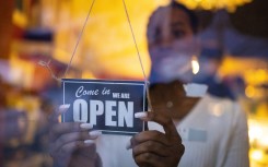 File: A woman turning an open sign on glass front door of a coffee shop. Getty Images/Luis Alvarez