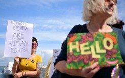 People hold up placards to welcome migrants to the barge which the government insists is a cost-effective option