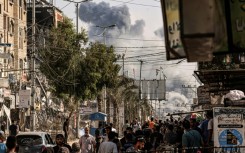 People walk along a street as a plume of smoke rises in the background during a strike on the Bureij refugee camp in the central Gaza Strip on November 2, 2023