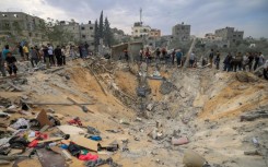 People stand over a crater following Israeli bombardment in the southern Gaza Strip 