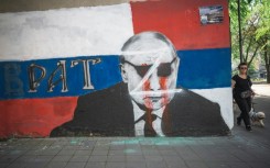 A woman walks past a vandalised mural of Russian President Vladimir Putin in Belgrade