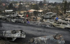 Survivors walk past burned out vehicles after a wildfire ravaged Quilpue, in Chile's Vina del Mar region