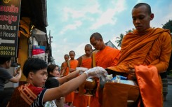 Monks have to make their way through hundreds of visitors on plastic stools offering alms as tour guides thrust mobile phones into their faces