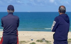 Palestinian men watch the Open Arms charity vessel bringing the first shipment of food aid to Gaza via a new maritime corridor from Cyprus