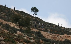 Armed Israeli settlers gather on a hill overlooking Al-Mughayyir village