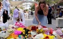 People react as they leave flowers outside the Westfield Bondi Junction shopping mall in Sydney on April 14, 2024