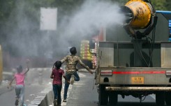 Children run behind a truck spraying water along a street on a hot summer day in New Delhi on Tuesday