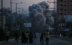 Palestinians watch smoke billowing following an Israeli air strike in Deir al-Balah