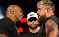 Mike Tyson, left, and Jake Paul, right, stare at each other while promoter Nakisa Bidarian, center, looks on ahead of their heavyweight boxing showdown, which has been rescheduled for November 15