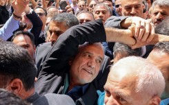 Iranian reformist presidential candidate Masoud Pezeshkian (C) greets supporters outside a polling station in Tehran during the runoff