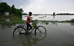 A boy pushes his bicycle through a flooded part of Jhargaon village in Morigaon district, Assam