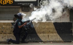 A Bangladesh policeman fires tear gas shells at protesters during clashes in Dhaka