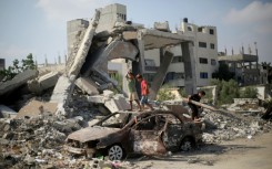 Palestinian children play on the wreckage of a car near a building destroyed in Israeli bombardment, in central Gaza's Al-Bureij refugee camp