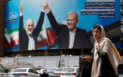 A woman walks past a picture of Iranian President Masoud Pezeshkian (R) and slain Hamas leader Ismail Haniyeh in Tehran