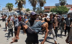 A Palestinian carries a man wounded in Israeli bombardment in Deir el-Balah