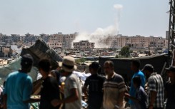 Displaced Palestinians watch from a makeshift camp as Israeli shelling hits Khan Yunis in the southern Gaza Strip