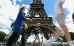 Pedestrians walk past the Eiffel Tower adorned with the Olympic Rings ahead of the 2024 Olympic Games in Paris in July 16, 2024.