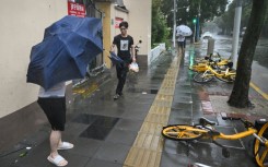 People walk past fallen bicycles amid strong winds and rain from Typhoon Bebinca