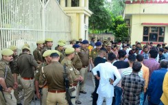 Policemen stand guard as mourners protest after newborns died in a hospital blaze in Jhansi 