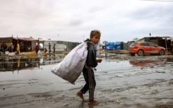 A displaced Palestinian child carrying a bag walks barefoot in a displacement camp in the central Gaza Strip 