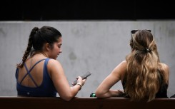 Two women sit on a bench looking at their phone in central Sydney. The Australian government says a new law aims to protect young people from the perils of social media