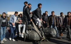 Damascus University students stand on a toppled statue of Syria's late president Hafez al-Assad during a rally near the campus