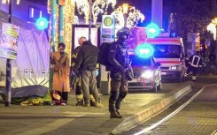 An injured person is lying on a stretcher as police and ambulances stand next to the Christmas market attack scene